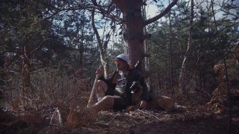 Handsome Man Sitting and Resting After Hardwork in The Forest With His Dog Stock Footage 87534851