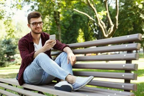 Handsome man sitting and using smartphone outdoors Foto stock