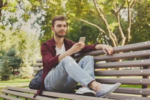 Handsome man sitting and using smartphone outdoors Stockfoto's