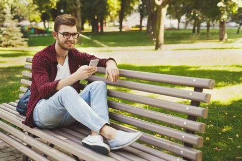 Handsome man sitting and using smartphone outdoors Stock Photos