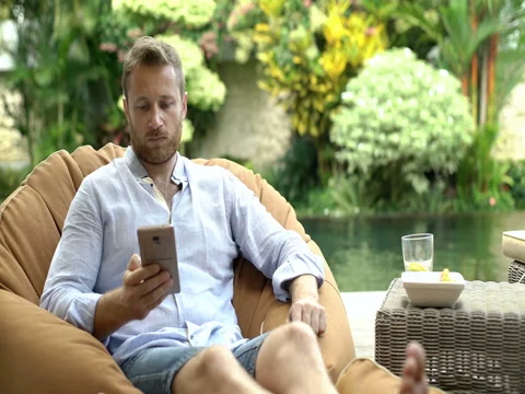 Handsome man sitting on bean bag chair and chatting on cellphone Stock-Footage 79225963