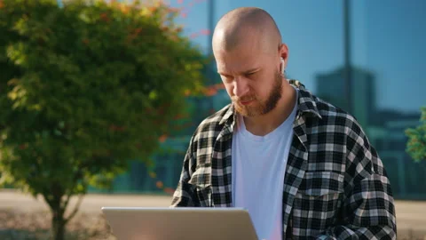 Handsome Man Sitting on the Bench Outside, Working on Laptop, Using Earphones Stock Footage 236716522