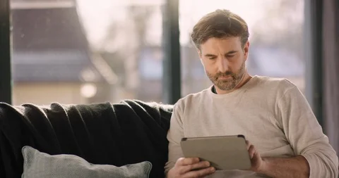 Handsome Man sitting on Coach using Tablet Computer Stock Footage 86478014