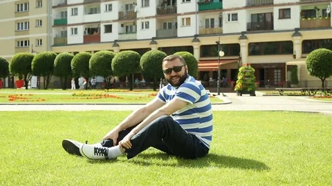 Handsome man sitting on the grass in the park and smiling to the camera Stock Footage 76981789