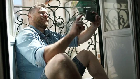 Handsome man sitting next to the bars and doing selfies on smartphone, steadycam Stock-Footage 76990940