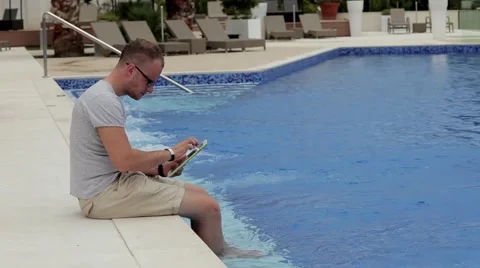 Handsome man sitting next to the pool with tablet pc Stock Footage 53569365
