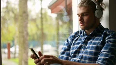 Handsome man sitting next to the window and listening music on headphones Stock Footage 75136828