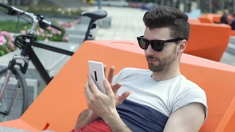 Handsome man sitting on the orange seat and browsing internet on smartphone, ste Stock Footage