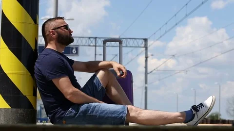Handsome man sitting on the platform and waiting for train arrival Stock Footage 78649944