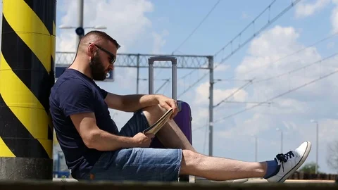 Handsome man sitting on the platform and reading book Stock Footage 78650066
