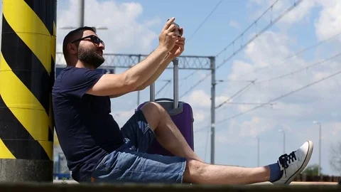 Handsome man sitting on the platform and doing selfies on smartphone Video stock 78650236