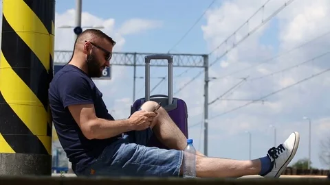Handsome man sitting on the platform and texting messages on smartphone Video stock 78650717