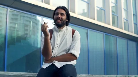 Handsome man sitting on the railing with a cigarette and smiling slow motion Stock Footage 79239938