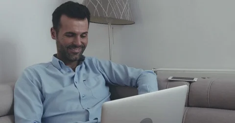 Handsome man sitting relaxed on couch using laptop and his phone Video stock 70311713