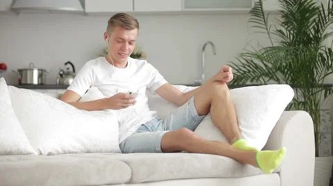 Handsome man sitting on sofa with cellphone and listening music Stock Footage 27692069