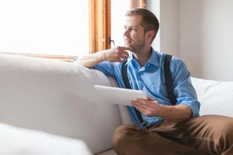Handsome man sitting on sofa using a digital tablet Stock Photos