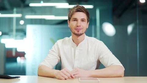 Handsome man sitting at workplace and looking at the camera. Smiling positive  Stock Footage 229086440