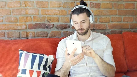 Handsome man smiling to the camera while listening music and using tablet 스톡 동영상 75953679