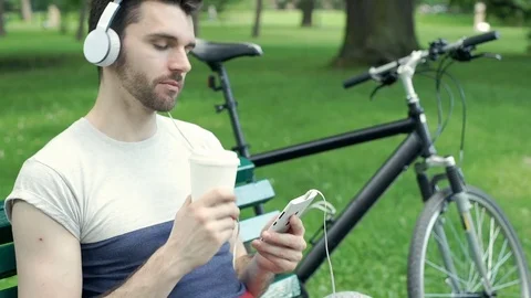 Handsome man smiling to the camera while listening music and drinking coffee in  스톡 동영상 77033379