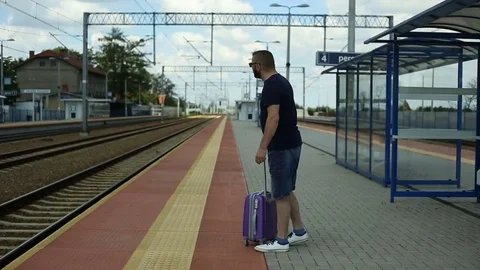 Handsome man smiling to the camera while holding luggage and waiting for train Stock Footage 78655749