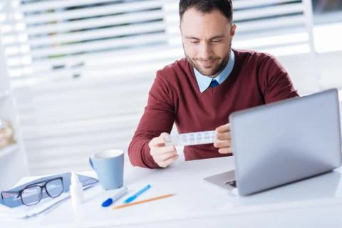 Handsome man smiling while looking at the tiny pillbox in his hands Foto stock