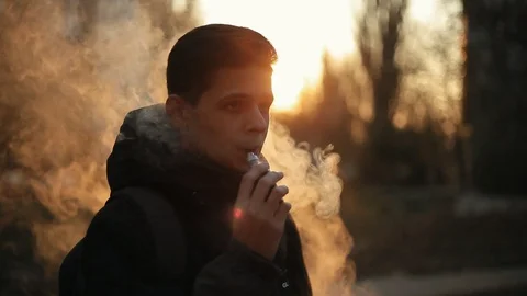 Handsome man smoking e-cig on the street at sunset.Closeup Video stock 98749631