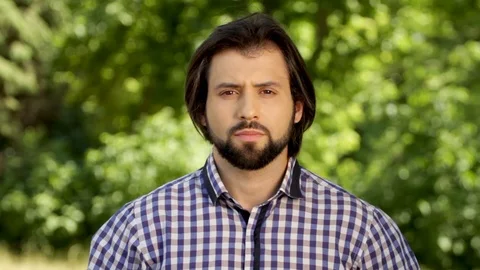 Handsome man is standing and looking on camera. He looks serious for some time Stock-Footage 99740271