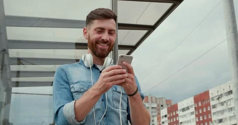 Handsome Man Standing at the Bus stop with Mobile Phone, Using social Media. Stock Footage 122996492
