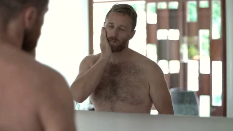 Handsome man standing in front of the mirror in the bathroom and shaving his bea Stock Footage 81085730
