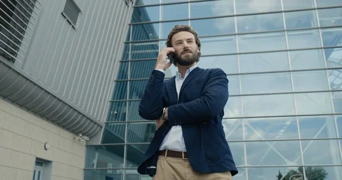 Handsome Man is stylish clothes is talking on his Phone near modern Building Video stock 124017453