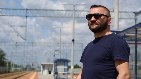 Handsome man in sunglasses waiting on the platform and smiling to the camera Stock Footage 78655140