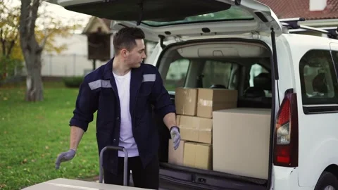 Handsome man takes boxes out of trunk and places them in a handcart. Parcel Stock Footage 168412083