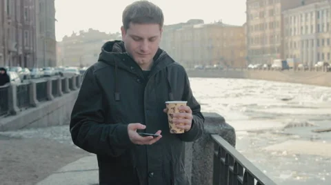 Handsome man talking on a mobile cell phone and enjoying a hot drink on the Stock Footage 61875479