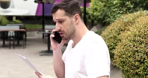 Handsome man talking smartphone with paper document. Stock Footage 247239725