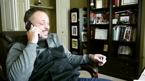 Handsome man talks laughs over the smart phone with his friend Stock Footage 77573759