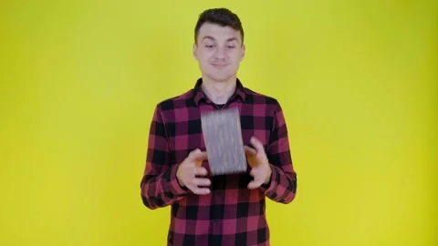 Handsome man throws box with gift from hand to hand on yellow background Stock Footage 132381314