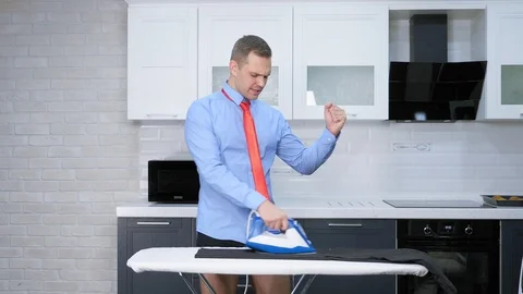 Handsome man in tie ironing pants . the kitchen of his house Stock Footage 125709481
