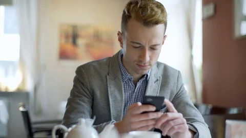 Handsome man in a tweed jacket looks happy while browsing internet on smartphone Stock Footage 70684643