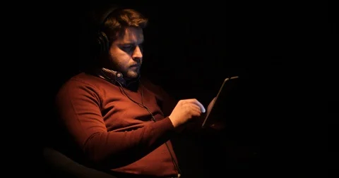 A handsome man uses a tablet and listens music in a dark room Stock Footage 88058891
