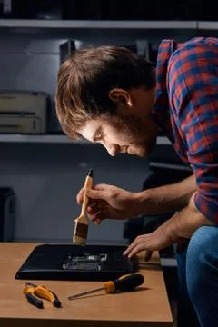 Handsome man using brush to clean the laptop from the dust Stock Photos