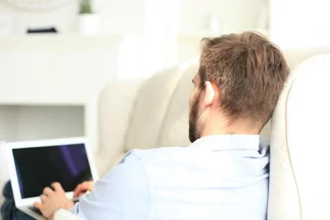 Handsome man is using a digital tablet and smiling while resting on couch. Stock Photos