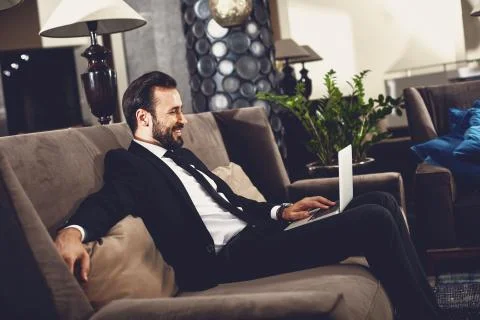 Handsome man using his laptop in the hall and looking glad Foto stock
