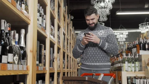 Handsome man using his smart phone while shopping at wine store Stock-Footage 147408019