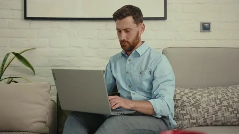 Handsome man using laptop typing working sitting on couch in modern living room Stock Footage 132539589