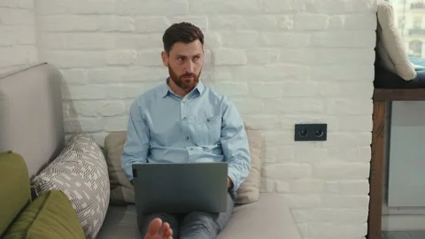 Handsome man using laptop typing working lying on couch in modern living room at Stock Footage 132539764