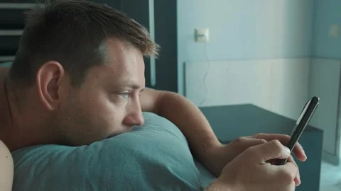 Handsome man using mobile phone in bed at the morning surfing internet, checking Stock Footage 250117137
