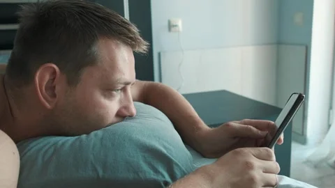Handsome man using mobile phone in bed at the morning surfing internet, checking Stock Footage 252131354