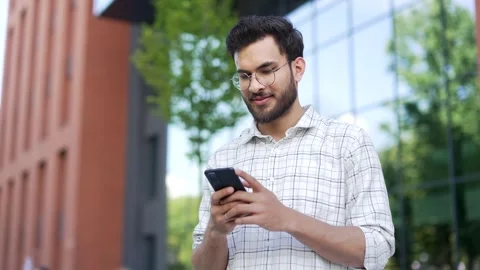 Handsome man is using a mobile phone while standing on the street near an modern Stock Footage 306299774