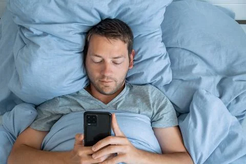 Handsome man using mobile phone in bed at the morning surfing internet, checking Stock Photos