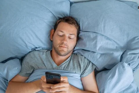 Handsome man using mobile phone in bed at the morning surfing internet, checking Stock Photos